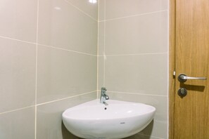 A bathroom with a white sink, a wooden door, and tiled walls. - Strategic Studio Apartment At B Residence Near Campus (Pagedangan)