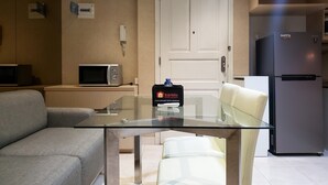 A modern living room with a glass-top table, a sofa, a refrigerator, and a microwave.