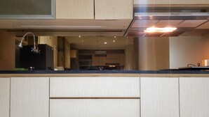 A modern kitchen with light wood cabinetry, a stainless steel range hood, and a black countertop.