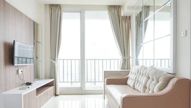 A modern living room with a sofa, TV, and a balcony with curtains.