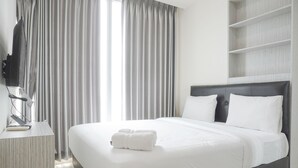 A neatly made bed with white linens, a flat-screen TV on a bedside table, and a large window with curtains.