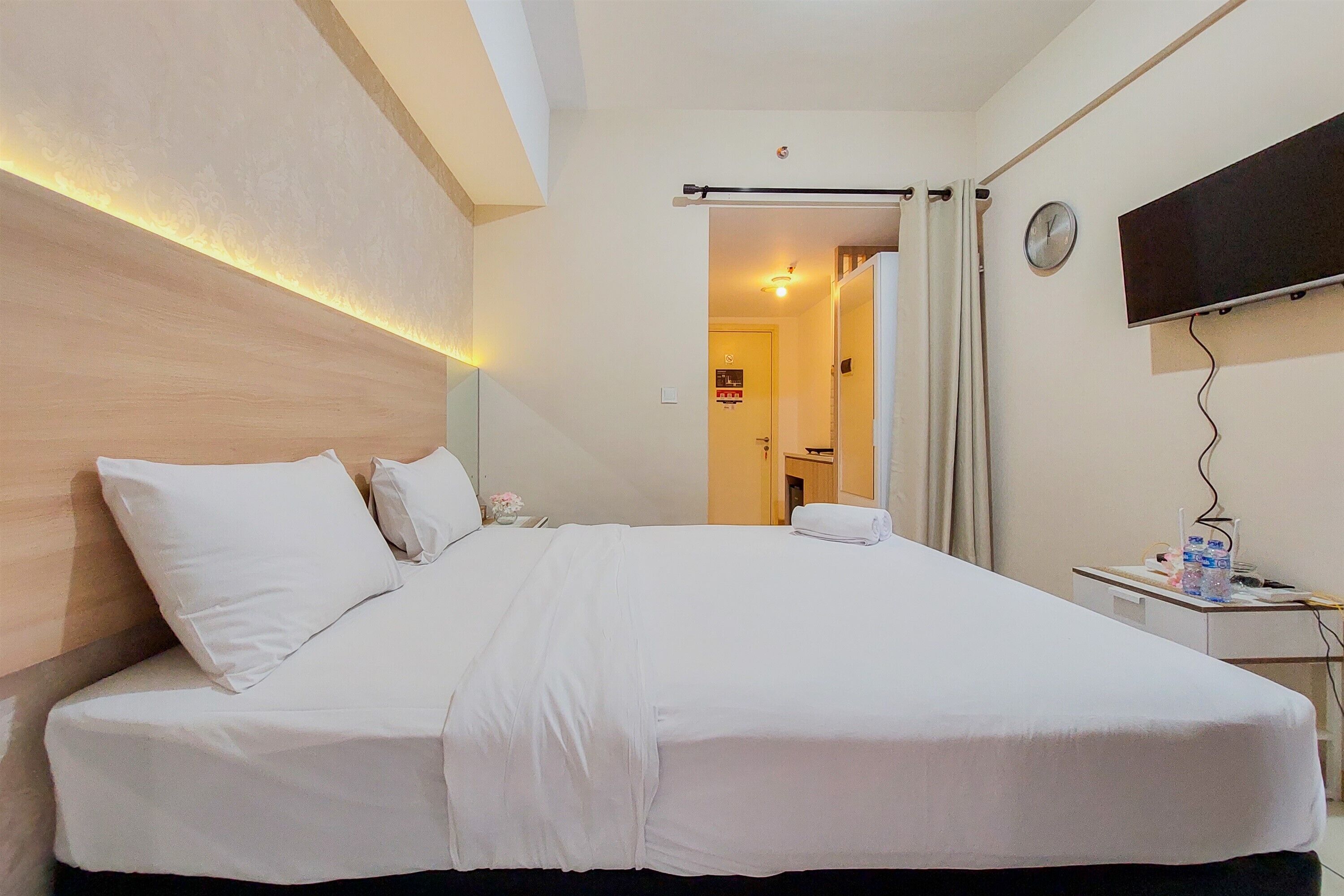 A hotel room with a large bed, a flat-screen TV mounted on the wall, a bedside table with a lamp, and a door leading to a bathroom.