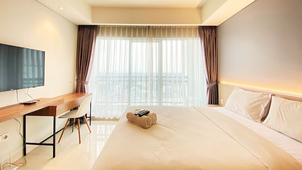 Een hotelkamer met een bed, een bureau, een televisie en uitzicht op de stad door grote ramen.