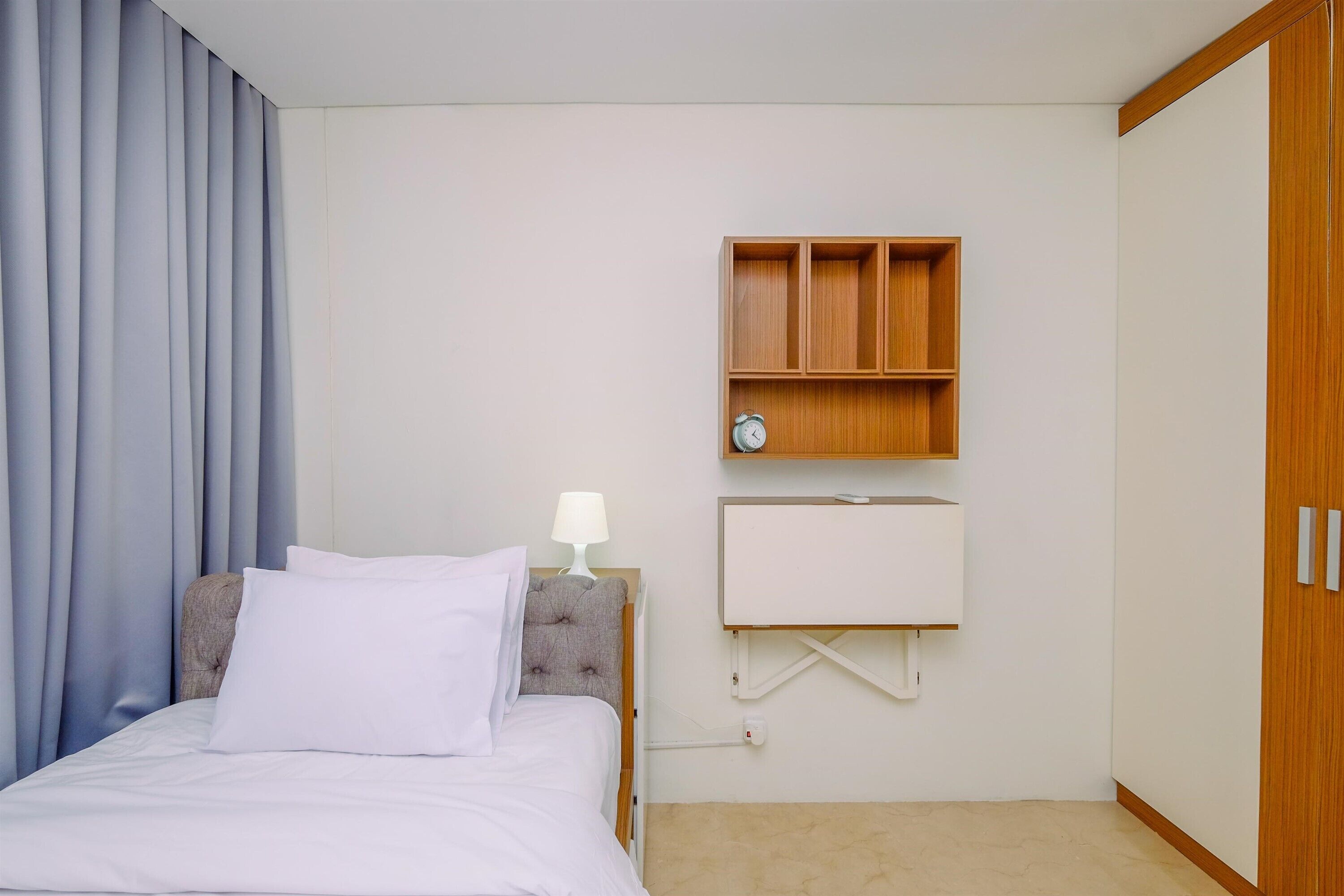 Habitación de hotel con cama, mesita de noche, estante en la pared con un reloj y armario.