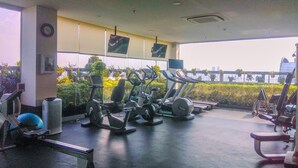 A gym with various exercise equipment, large windows, and a view of greenery and buildings. - Elegant And Nice 2Br At L'Avenue Pancoran Apartment (Jakarta)