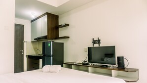 Una habitación de hotel con cama, escritorio, computadora, televisor, barra de minibar y puerta.