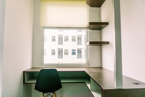 A corner room with a window overlooking a building, a desk, and a chair. - Nice And Comfort Studio Room At Serpong Garden Apartment (Cisauk)