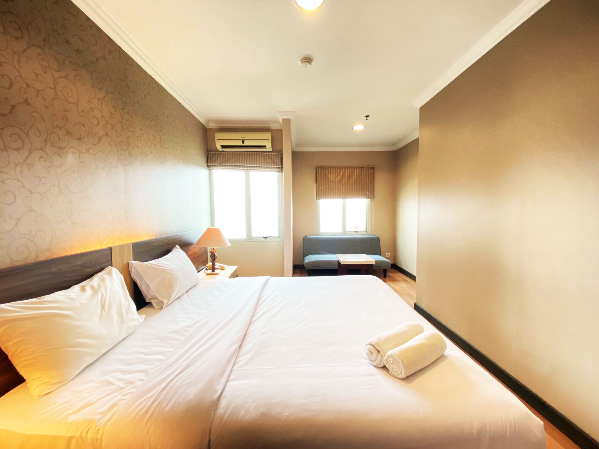 Habitación de hotel con una cama grande, una mesita de noche con lámpara, una ventana con cortinas y un equipo de aire acondicionado.