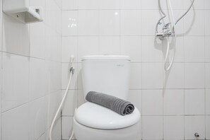 A bathroom with a white toilet, a towel, and a shower fixture.