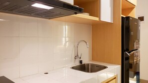 A modern kitchen with white tiles, stainless steel sink, and a black refrigerator. - Minimalist And Tidy 2Br Apartment At Tokyo Riverside Pik 2 (Teluknaga)