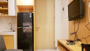 A compact kitchen with a black refrigerator, a wooden cabinet, a sink, and a television mounted on the wall. - Minimalist And Tidy 2Br Apartment At Tokyo Riverside Pik 2 (Teluknaga)