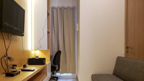 A compact room with a wooden desk, a television, a sofa, and a curtain-covered door. - Minimalist And Tidy 2Br Apartment At Tokyo Riverside Pik 2 (Teluknaga)