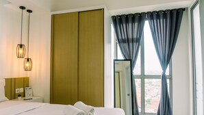 Ein Hotelzimmer mit Bett, Nachttisch, Lampe, Kleiderschrank und einem Fenster mit Vorhängen.