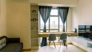 Ein modernes Wohnzimmer mit einer Couch, zwei Sesseln, einem Fernseher und einem Fenster mit Vorhängen.