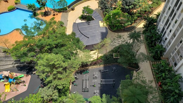 An aerial view of a hotel with a swimming pool, a children's play area, and a parking lot surrounded by greenery.