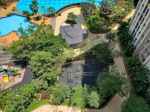 An aerial view of a hotel with a swimming pool, a children's play area, and a parking lot surrounded by greenery.