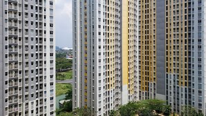 A high-rise residential building with multiple balconies, a central courtyard, and a view of a stadium in the background.