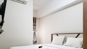 A neatly made bed with white linens, a remote control, and a rolled towel on it.