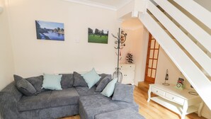 Un soggiorno moderno con un divano angolare grigio, un poggiapiedi, un tavolino bianco e una scala che conduce a un piano superiore.