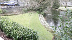 Una vista sul fiume con un sentiero in pietra che conduce a una zona erbosa, circondata da alberi e edifici sullo sfondo.