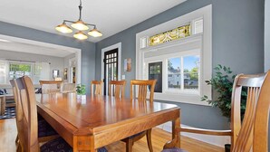A dining room with a wooden table and chairs, a chandelier, and a view through a window.
