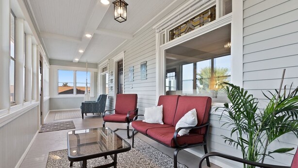 A covered porch with red and grey upholstered seating, a glass table, and a potted plant.