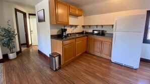 A kitchen with wooden cabinets, a stainless steel trash can, a white refrigerator, and a potted plant. - The Tiny Piney  - Live. Work. Play. Downtown Green Bay! (Green Bay)