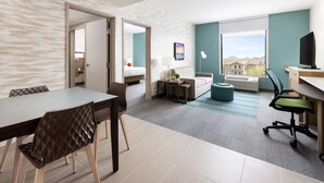 A modern hotel room with a dining area, a bed, a desk, and a view of the city. - Home2 Suites by Hilton Scottsdale North (Scottsdale)