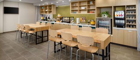 A modern cafe with wooden tables and chairs, a coffee machine, and shelves with various items.