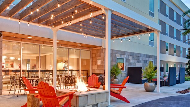 An outdoor seating area with fire pit, red Adirondack chairs, and a covered patio with string lights. - Home2 Suites by Hilton Scottsdale North (Scottsdale)