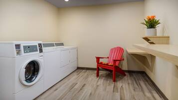A laundry room with a washing machine, a red chair, and a shelf with a potted plant.