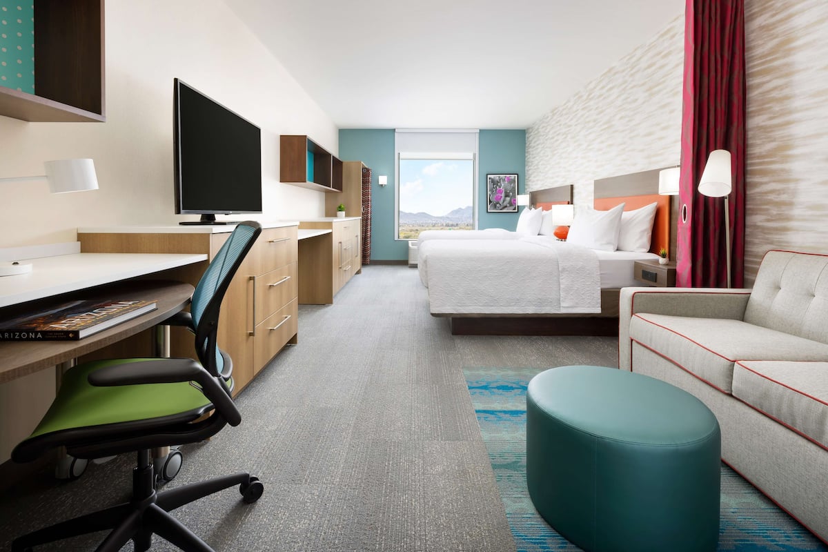 A hotel room with a bed, a desk with a computer, a chair, a sofa, and a TV.
