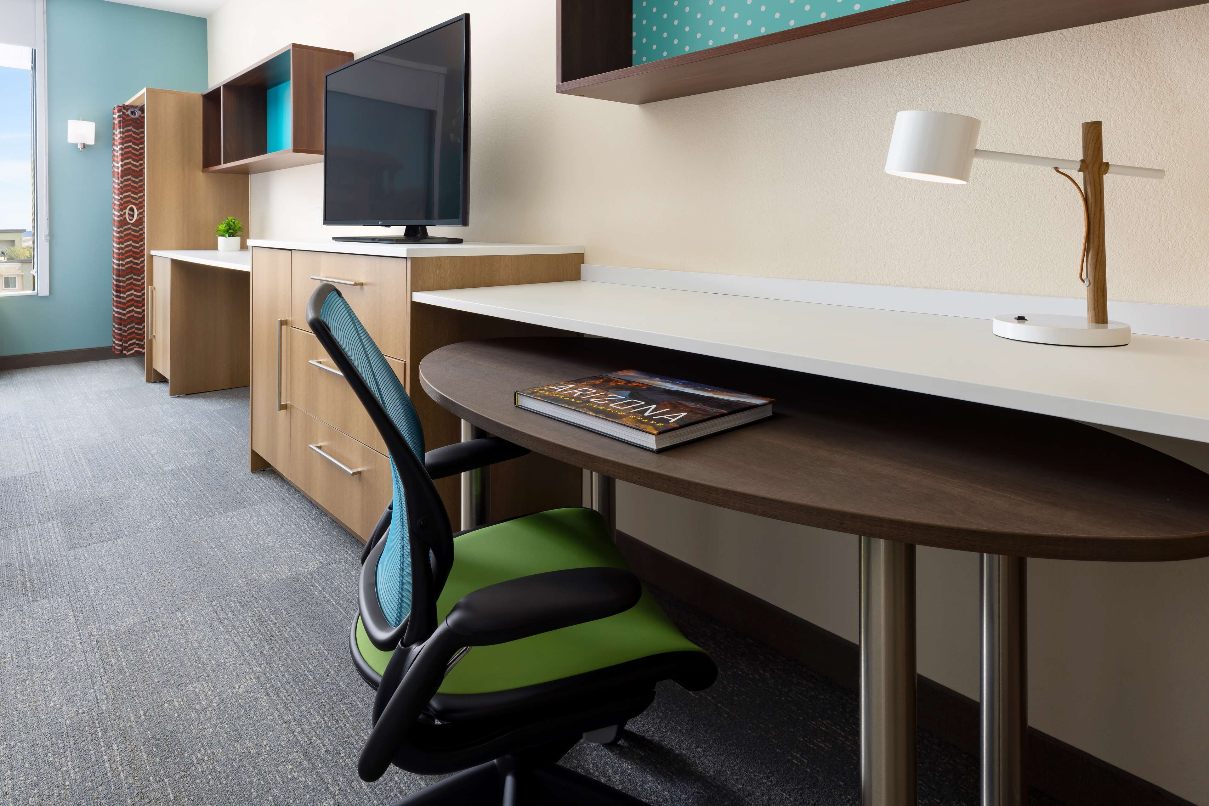 A modern office space with a desk, chair, TV, and a lamp.