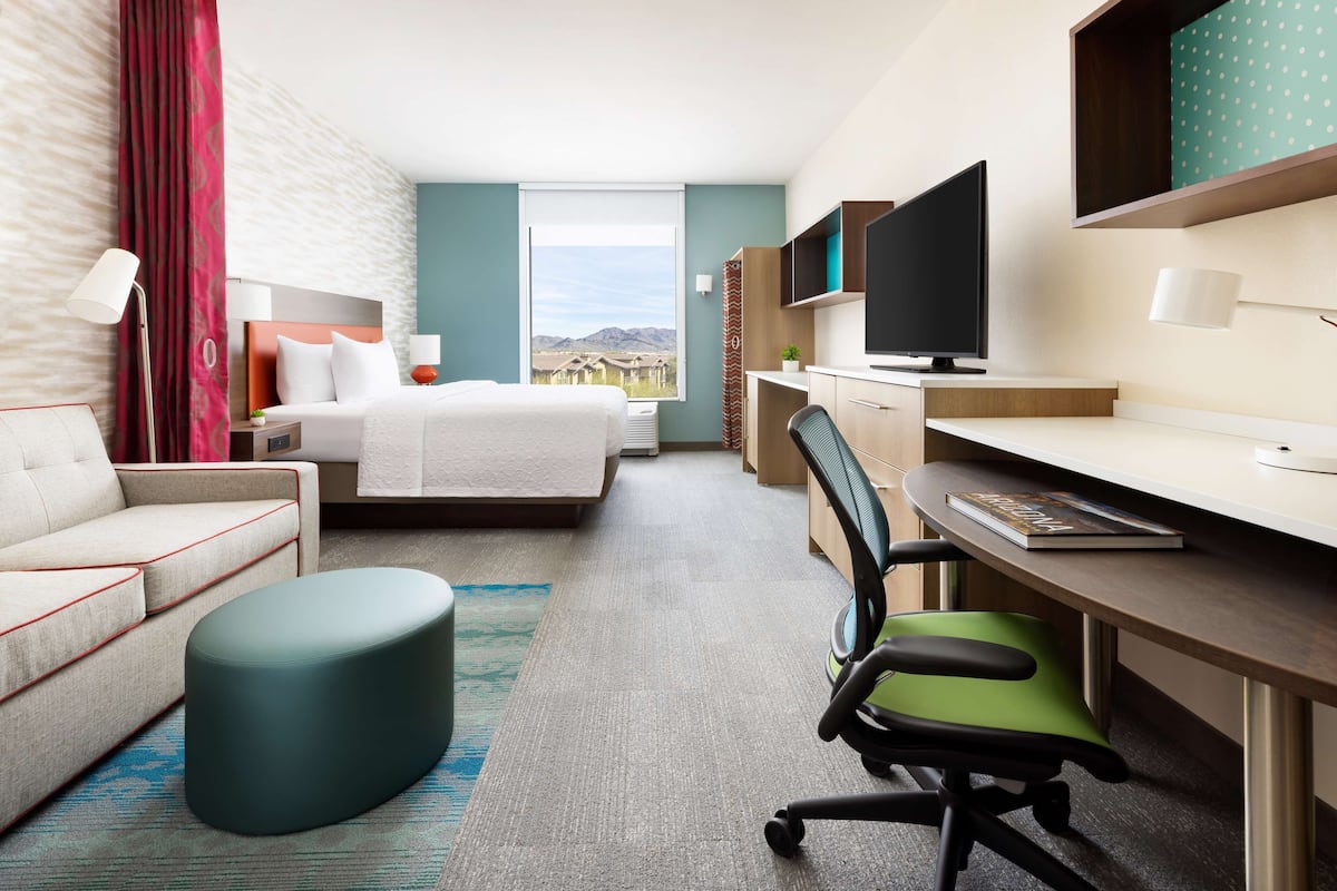A hotel room with a bed, a desk, a chair, a sofa, and a TV.