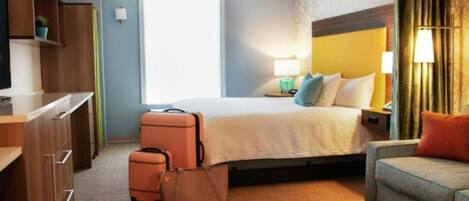A hotel room with a bed, a desk, a chair, a suitcase, and a handbag.