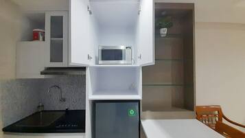 A compact kitchen with a microwave, a small refrigerator, a sink, and a dining area with a table and chairs.