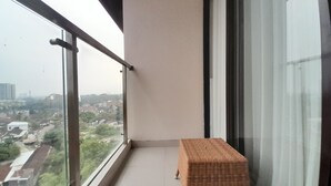 A balcony with a wicker bench, a glass railing, and a view of a cityscape. - Cozy Studio Room At Patraland Amarta Apartment (Ngaglik)