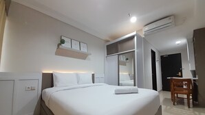 A modern hotel room with a neatly made bed, a desk with a chair, and a built-in wardrobe. - Cozy Studio Room At Patraland Amarta Apartment (Ngaglik)