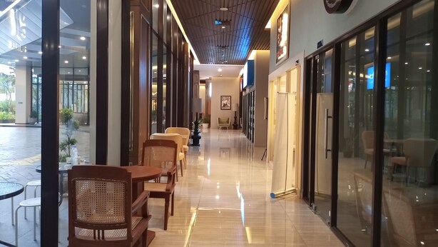A corridor with wooden flooring, glass doors, and seating areas with wicker chairs. - Cozy Studio Room At Patraland Amarta Apartment (Ngaglik)