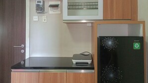 Une cuisine avec un réfrigérateur noir, des armoires en bois, un four à micro-ondes et une petite imprimante posée sur le comptoir.