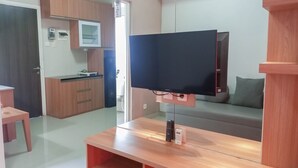 Un salon moderne doté d’un téléviseur à écran plat, de meubles en bois, d’un canapé et d’un coin cuisine avec des placards et un four à micro-ondes.