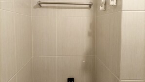 Une zone de douche carrelée, équipée d’une barre d’appui et d’un robinet fixé au mur.