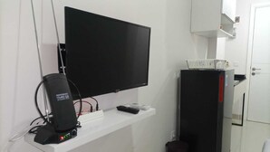 Une petite cuisine équipée avec un téléviseur fixé au mur, un réfrigérateur noir et un plan de travail blanc.