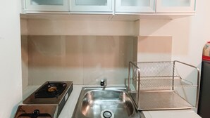 A small kitchen with a stainless steel sink, a stove, and a wire shelf. - Cozy And High Floor Studio Room At Vida View Makassar Apartment (Makassar)