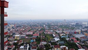 A high-rise building with multiple balconies overlooking a densely populated urban area with various buildings and greenery. - Cozy And High Floor Studio Room At Vida View Makassar Apartment (Makassar)