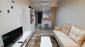 A modern living room with a flat-screen TV, a sofa, and a kitchen area in the background.