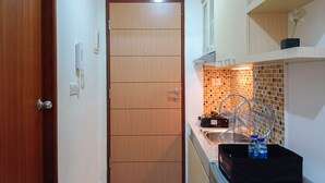 Une cuisine compacte avec une porte en bois, un pare-feu en carrelage et un petit plan de travail sur lequel se trouvent un panier et une bouteille d’eau.
