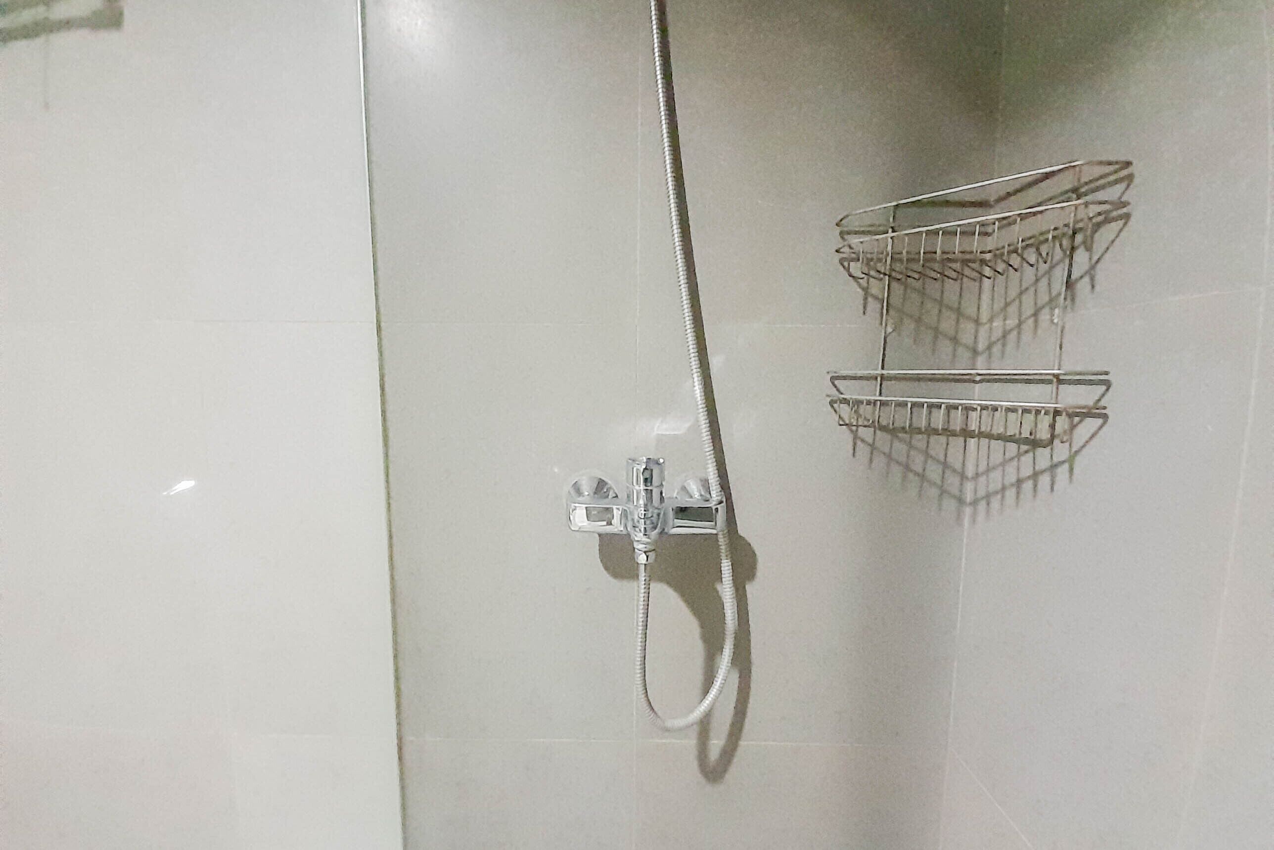 Une douche équipée d’un flexible et de deux paniers en métal fixés au mur.