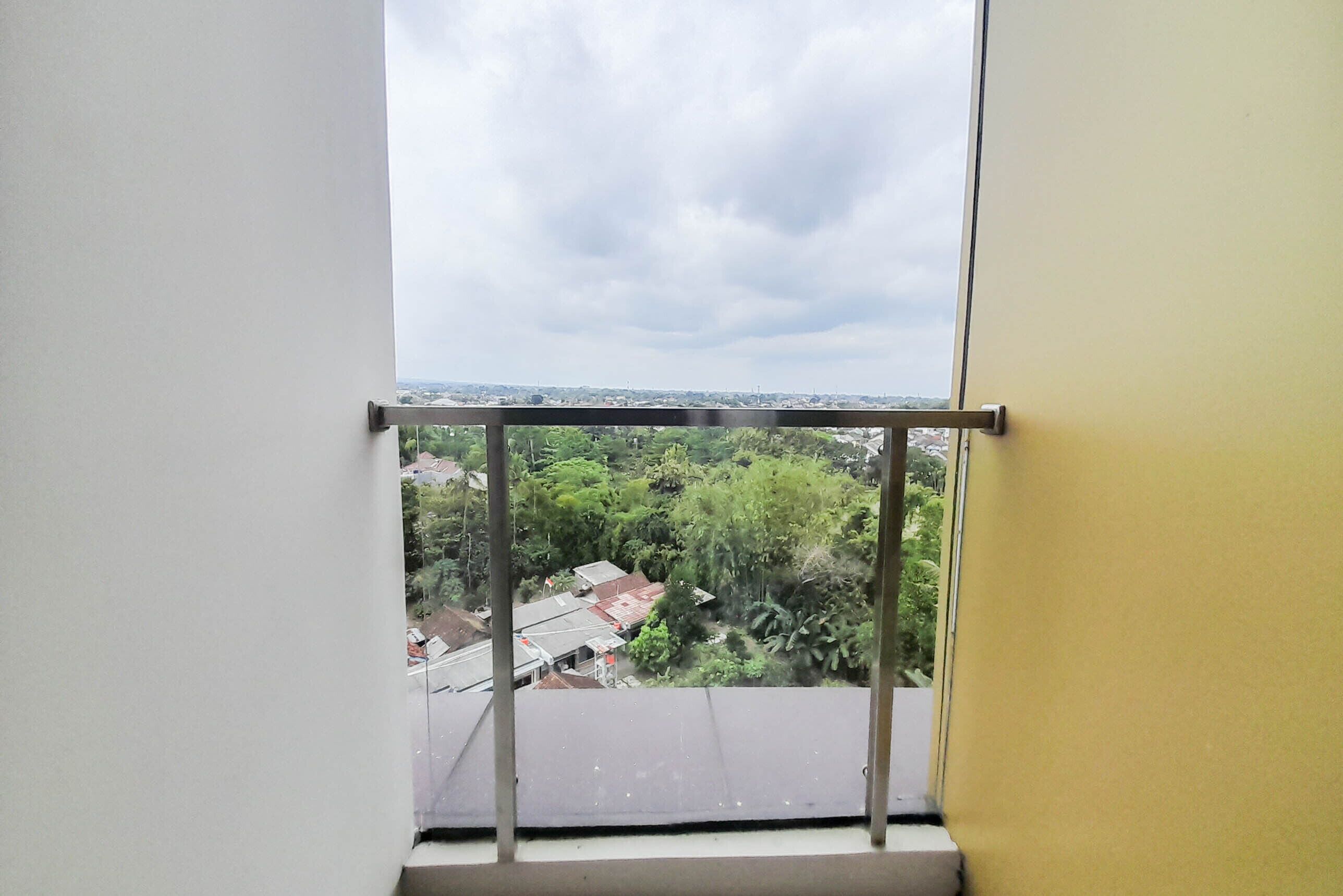 A window with a metal guard, overlooking a residential area with houses and greenery.