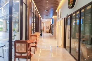 A corridor with wooden flooring, glass doors, and a seating area with wicker chairs and tables. - Fancy And Nice 1Br At Patraland Amarta Apartment (Ngaglik)